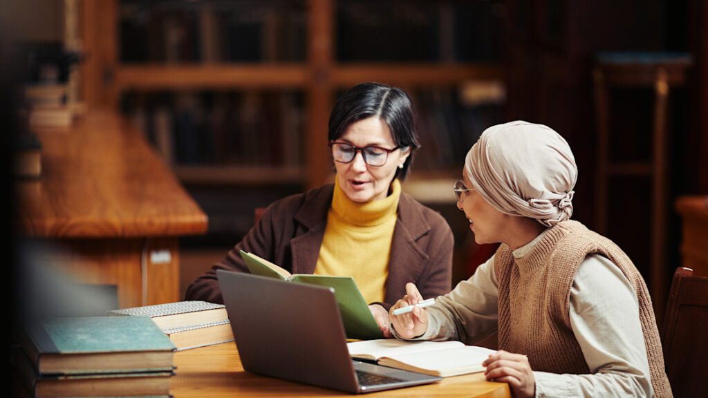 Horizontal warm toned portrait of two adult women studying together in classic college library copy.jpeg