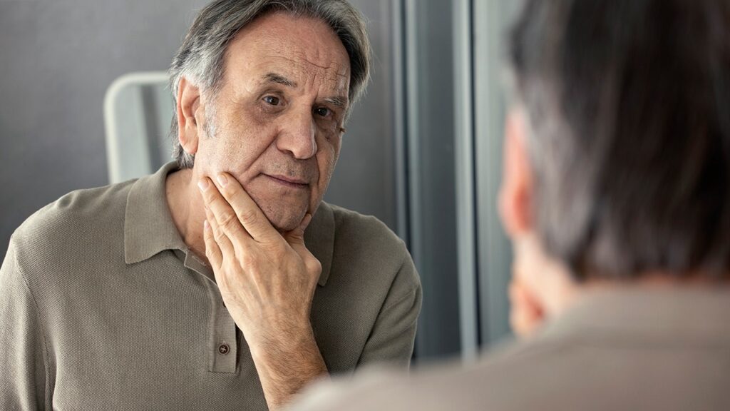 Older man looking in mirror at skin .jpg